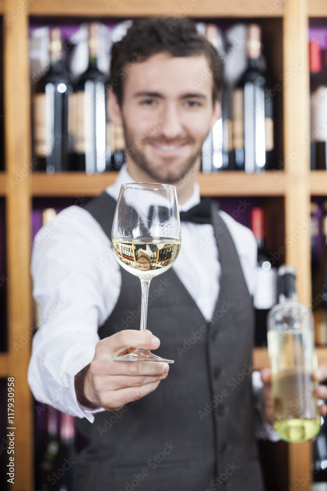 Bartender Offering White Wine Glass Against Shelves Bartender Offering White Wine Glass Against Shelves