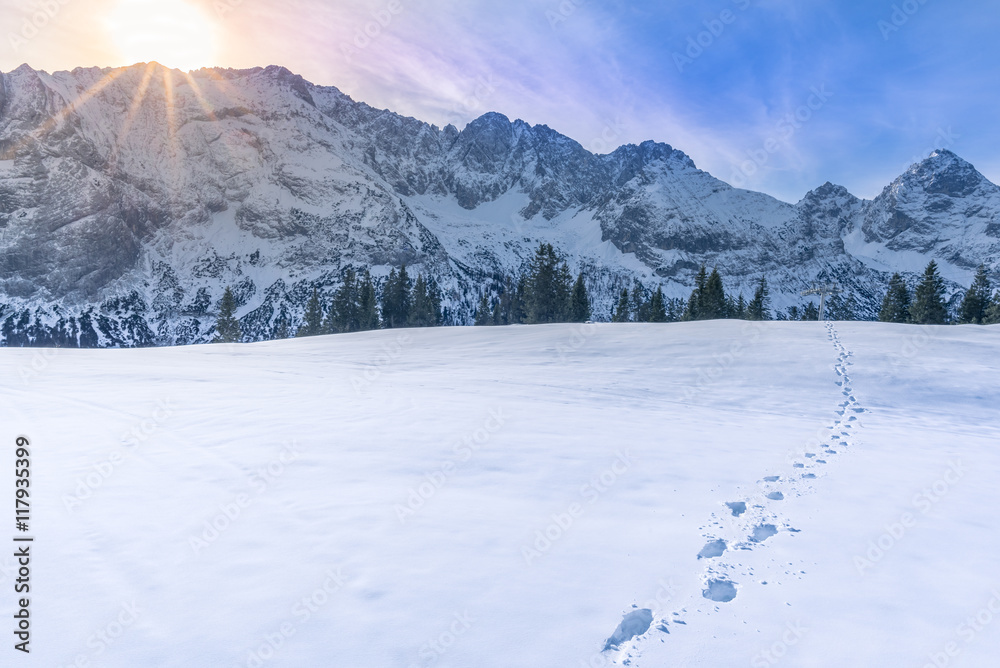Fototapeta premium Mountain peaks in winter Sunny, alpine landscape with the peaks of the Austrian Alps mountains on the horizon and a thick blanket of snow in the foreground, with footprints on it.