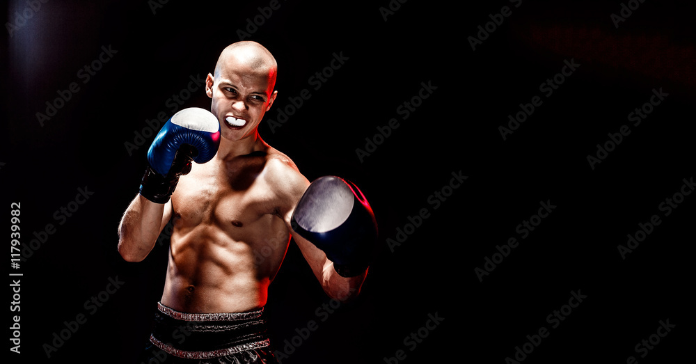 Muscular kickbox or muay thai fighter punching in darkness