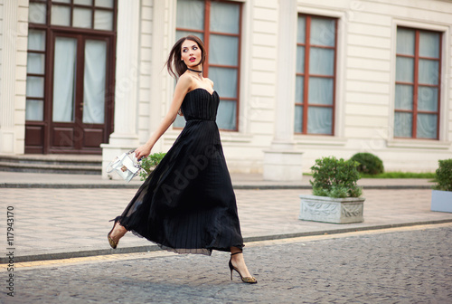 eautiful fashionable young woman in long dress running with bag.