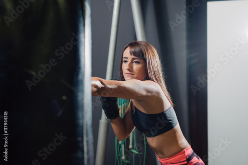 Young fit woman punching a boxing sack with gloves at the gym 