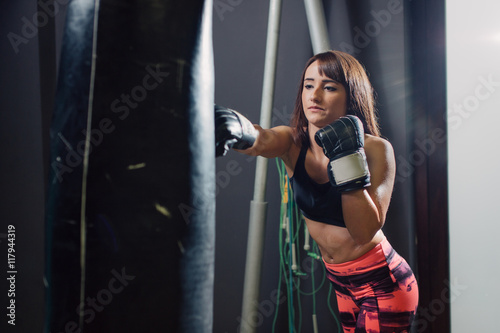 Young fit woman punching a boxing sack with gloves at the gym 
