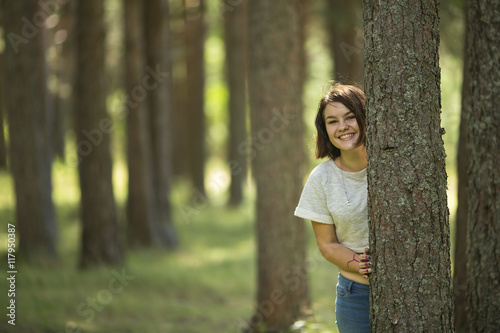 A teenage girl stands at a tree in the Park and smiles.