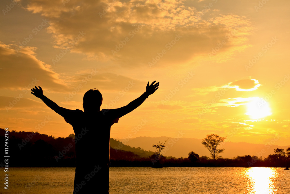 Man standing with his arms wide open at sunset