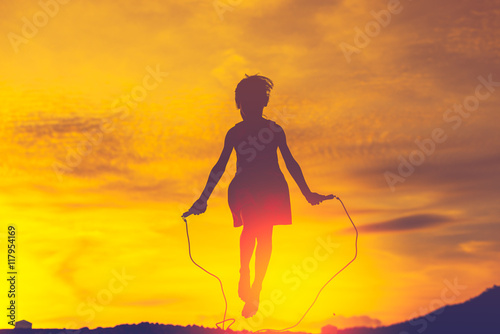 Girl jumping rope in silhouette with sun set