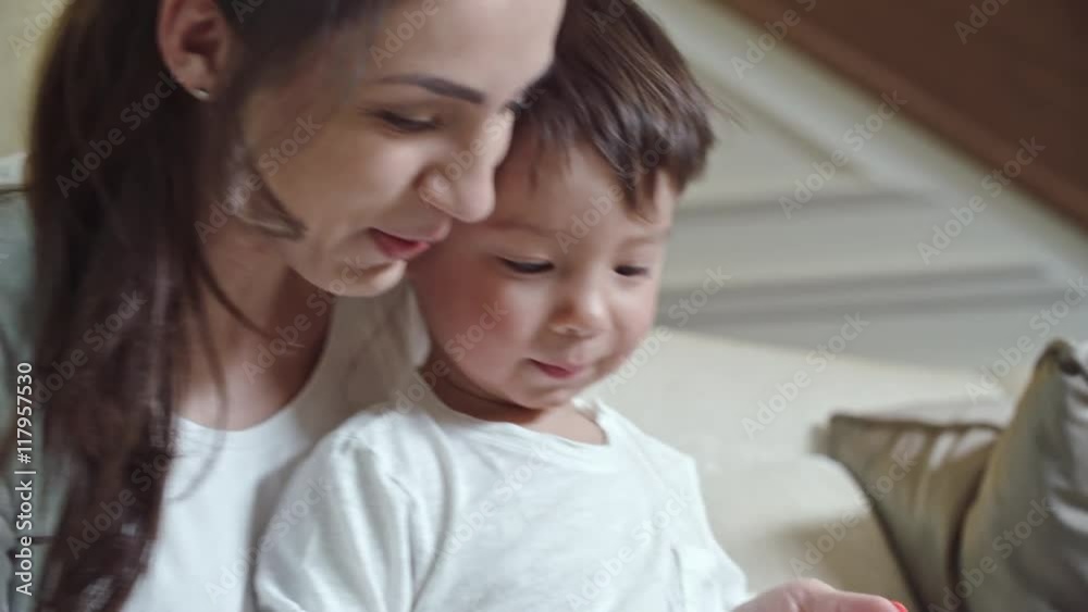 Cute boy sitting on his knees of his mother while she showing him something on tablet screen Cute boy sitting on his knees of his mother while she showing him something on tablet screen