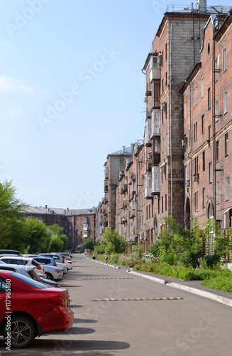 City yard. Courtyard urban apartment house in Russia. The house is brick, five-story, long. There are lawns with flowers and trees, asphalt and parking near the house. 