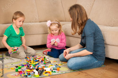 Children and their mother are playing with blocks on the ground