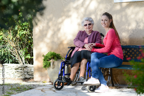 cheerful old woman in wheelchair with her young granddaughter outdoor in hospital