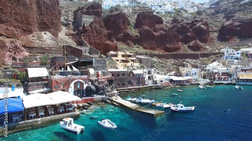 Aerial footage of Oia, Santorini - Famous white houses and blue domes on the edge of the cliff and blue lagoon.