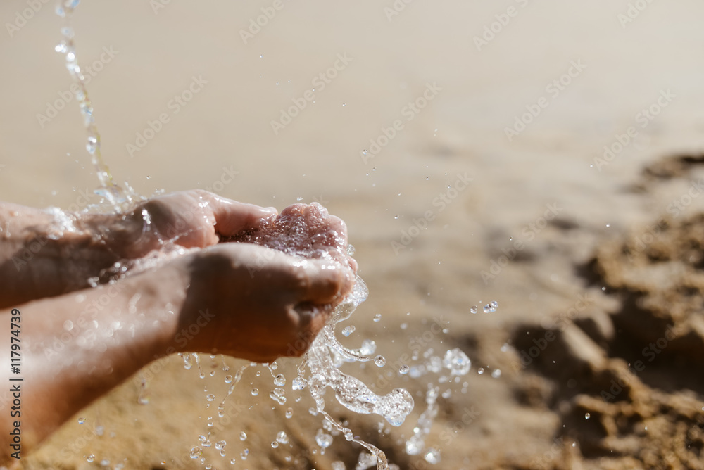 Fototapeta premium Person holding hands in splashes of water, sunny sandy outdoors background
