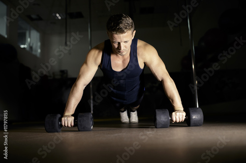 Young man doing pushups from dumbbell in gym