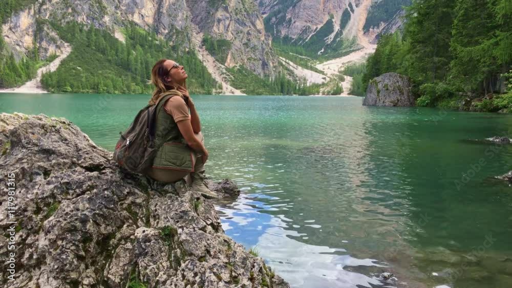 Woman hiker sitts on a cliff near Lago di Braies Woman hiker sitts on a cliff near Lago di Braies