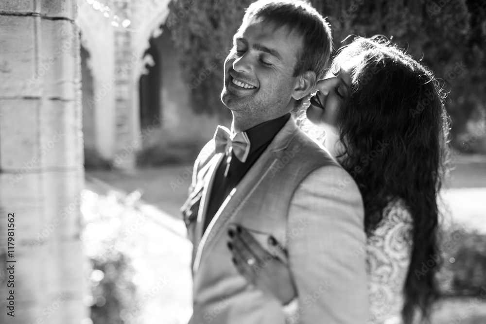 Black and white picture of a groom smiling while bride leans to Black and white picture of a groom smiling while bride leans to