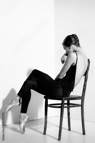 Ballerina in black outfit posing on a wooden chair, studio background.