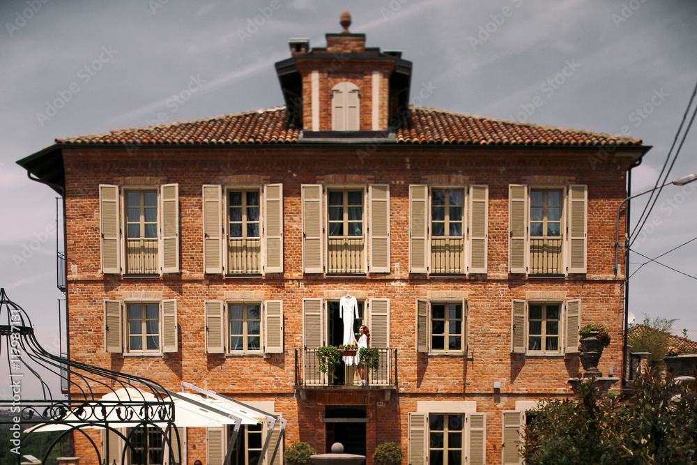 Fototapeta premium Woman stands before a wedding gown hanging on the balcony
