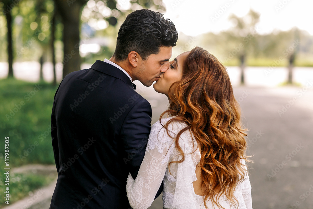 Look from behind at a tender kiss of stylish wedding couple