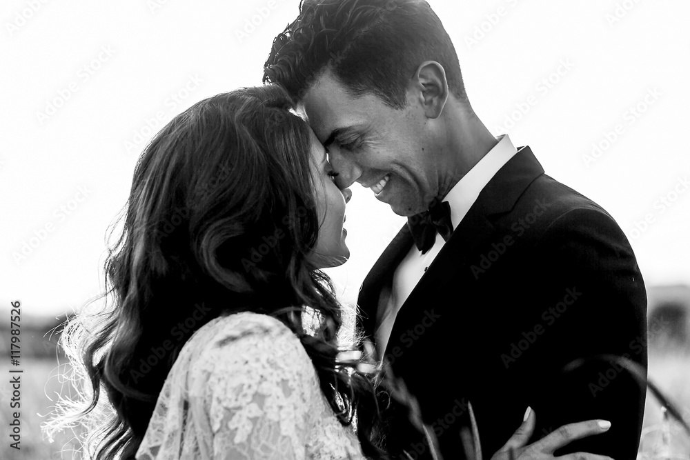 Smiling groom leans to bride's forehead standing with her in hig Smiling groom leans to bride's forehead standing with her in hig