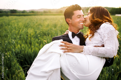 Italian groom carries elegant bride through the field