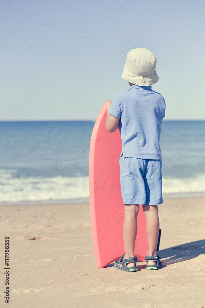 Back view of young man looking at the ocean on sunny beach, holding bodyboard