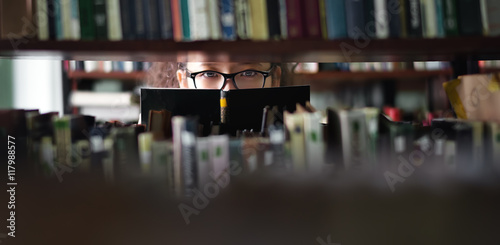 Portrait of clever student with open book reading it in college library