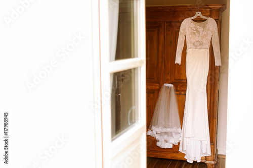 White dress and short veil hang on the wooden door