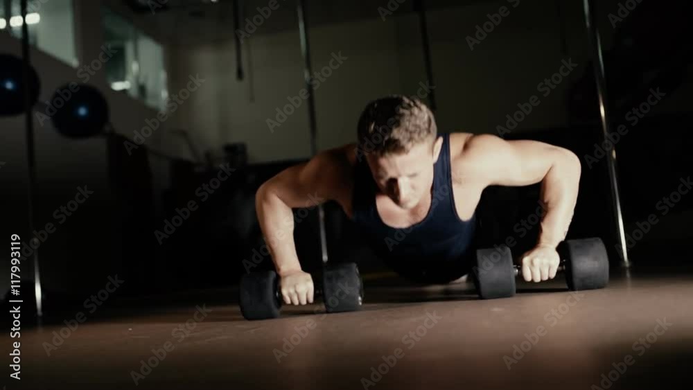 Athletic man doing push ups from dumbbells in gym