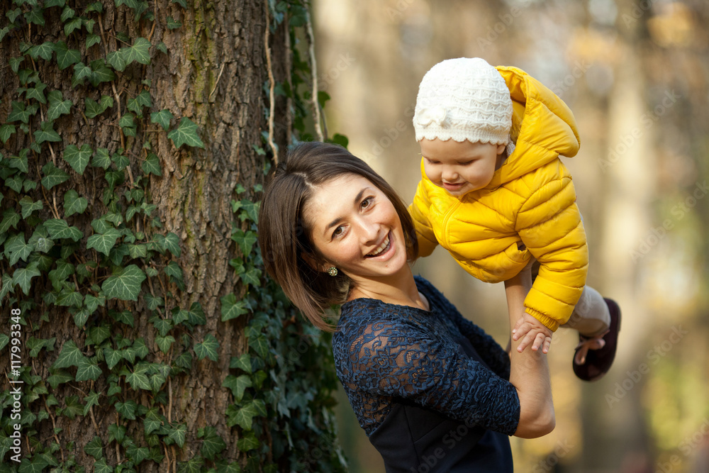 Fototapeta premium Mother smiles holding her little daughter in her hands