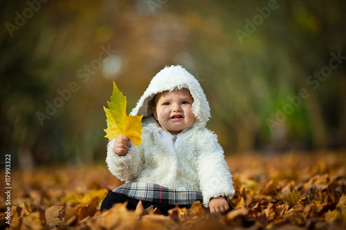 Girl in white coat holds a yellow leaf in her little arm