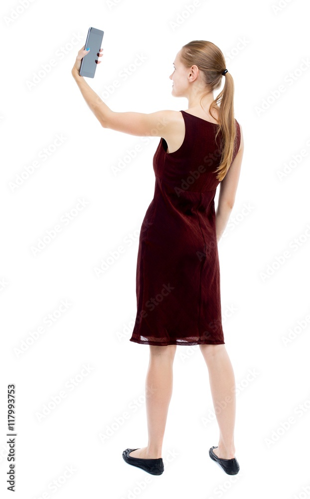 back view of standing young beautiful girl with tablet computer in the hands of. girl watching. Rear view people collection. backside view of person. Isolated over white background. The blonde back view of standing young beautiful girl with tablet computer in the hands of. girl watching. Rear view people collection. backside view of person. Isolated over white background. The blonde