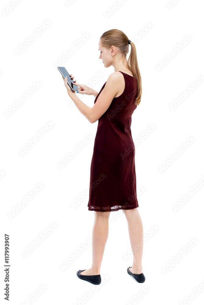 back view of standing young beautiful girl with tablet computer in the hands of. girl watching. Rear view people collection. backside view of person. Isolated over white background. The blonde back view of standing young beautiful girl with tablet computer in the hands of. girl watching. Rear view people collection. backside view of person. Isolated over white background. The blonde