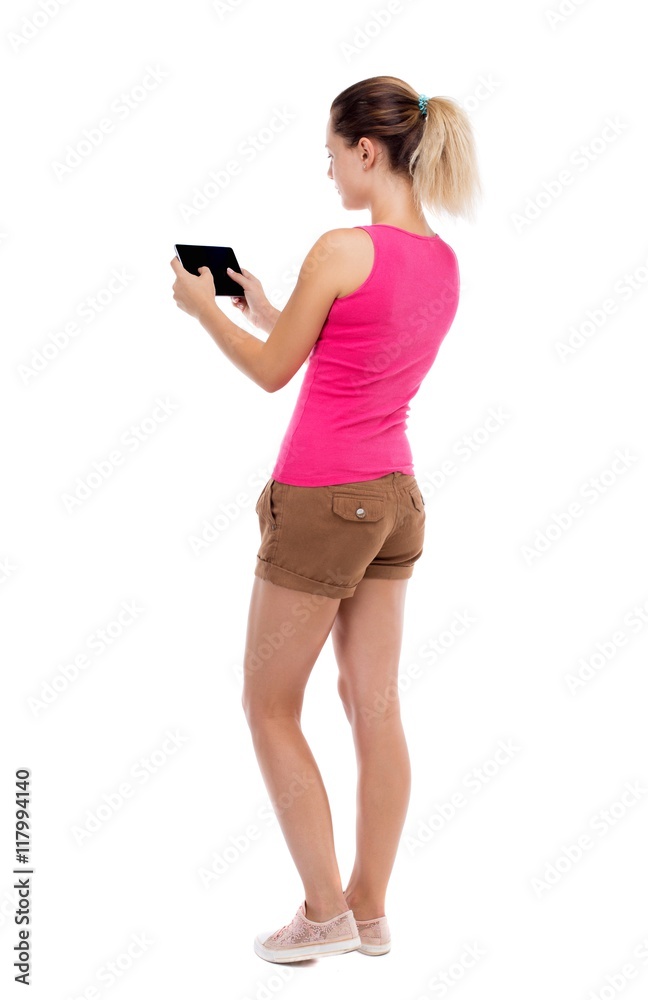 back view of standing young beautiful girl with tablet computer in the hands of. girl watching. Rear view people collection. backside view of person. Isolated over white background. Blonde in back view of standing young beautiful girl with tablet computer in the hands of. girl watching. Rear view people collection. backside view of person. Isolated over white background. Blonde in