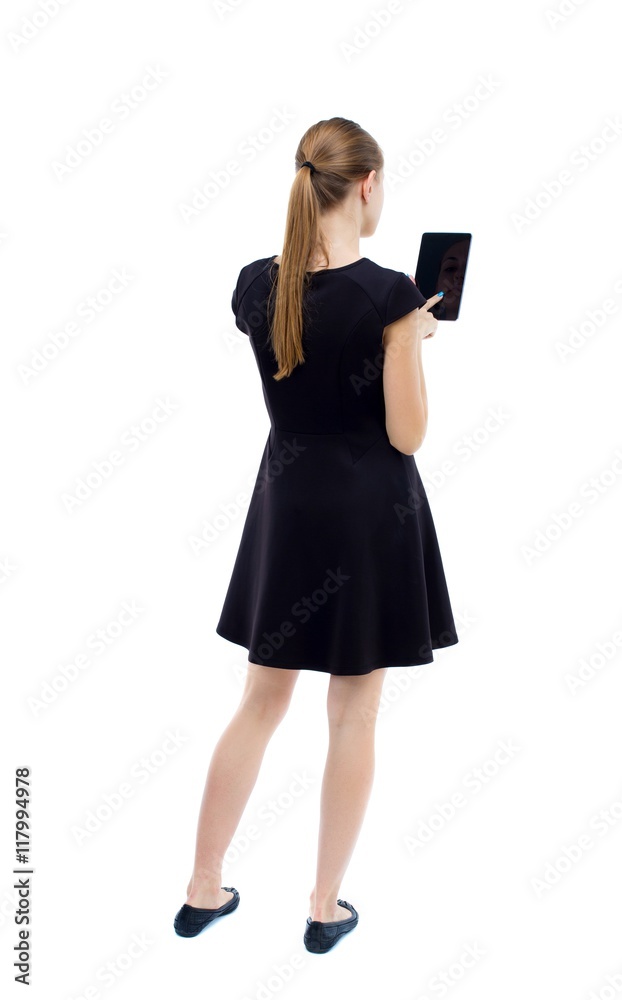 back view of standing young beautiful girl with tablet computer in the hands of. girl watching. Rear view people collection. backside view of person. Isolated over white background. The blonde in back view of standing young beautiful girl with tablet computer in the hands of. girl watching. Rear view people collection. backside view of person. Isolated over white background. The blonde in