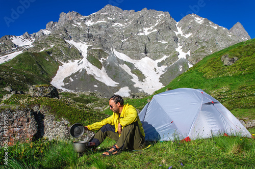 Young man preparing to eat on burner near the tent in the mountains of Georgia