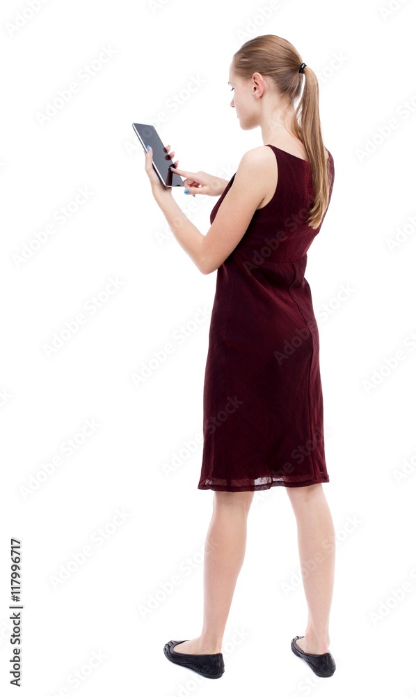 back view of standing young beautiful girl with tablet computer in the hands of. girl watching. Rear view people collection. backside view of person. Isolated over white background. The blonde back view of standing young beautiful girl with tablet computer in the hands of. girl watching. Rear view people collection. backside view of person. Isolated over white background. The blonde