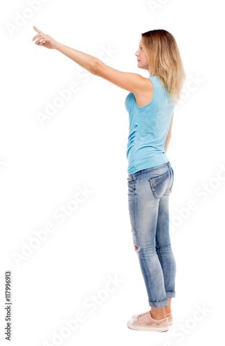 Back view of pointing woman. beautiful girl. Rear view people collection. backside view of person. Isolated over white background. The girl in jeans and a blue t-shirt standing sideways and shows a