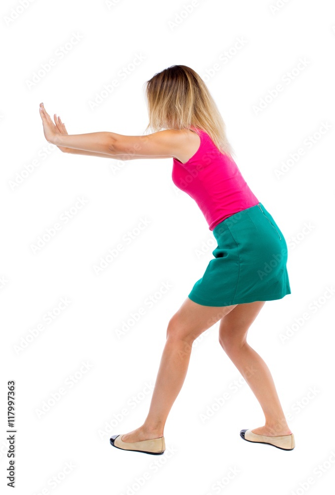 back view of woman pushes wall. Isolated over white background. Rear view people collection. backside view of person.The blonde in a green skirt and pink blouse rests his hands on the wall. back view of woman pushes wall. Isolated over white background. Rear view people collection. backside view of person.The blonde in a green skirt and pink blouse rests his hands on the wall.