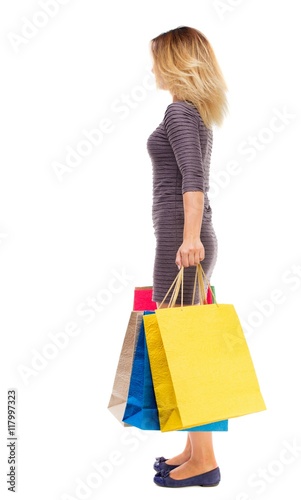 back view of woman with shopping bags . beautiful brunette girl in motion. backside view of person. Rear view people collection. Isolated over white background. Girl in purple dress is standing