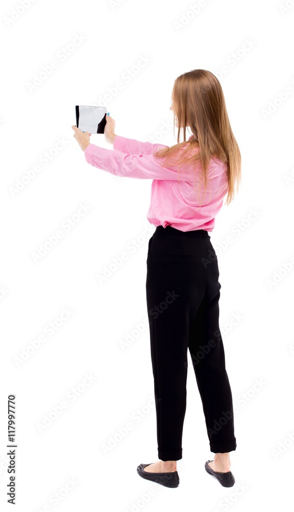 back view of standing young beautiful  girl with tablet computer in the hands of. girl  watching. Rear view people collection.  backside view of person.  Isolated over white background. The girl