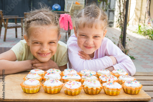 Two girls pretending funny faces  sitting in front of easter cupcakes