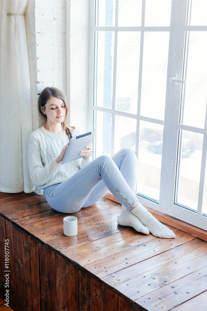 Beautiful woman using tablet while sitting on window Beautiful woman using tablet while sitting on window
