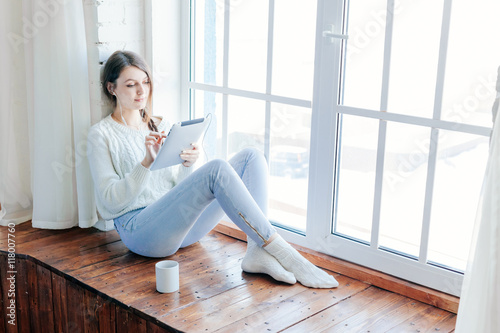 Beautiful woman using tablet while sitting on window
