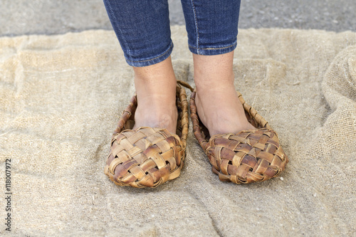 Feet girl in old Russian bast shoes are on canvas, which lies on the road. 