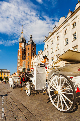 Church of St. Mary in the main Market Square with beautifully decorated horse and white old coach in the foreground. Basilica Mariacka. Krakow. Poland.