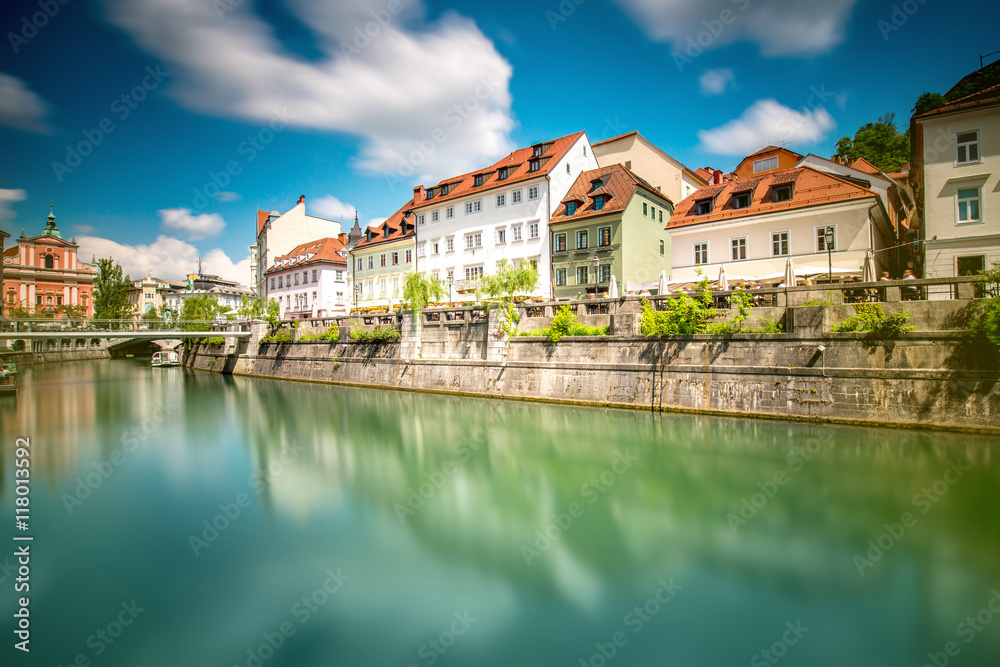 Fototapeta premium View on Ljubljanica river with old building in Ljubljana city in Slovenia. Long exposure image technic with blurred clouds and reflection on the water