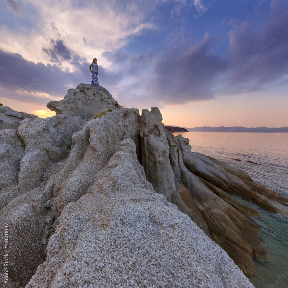 Fototapeta premium Single girl watching sunset high up on cliff by sea