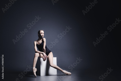 Young ballerina in a black suit is dancing in a dark studio