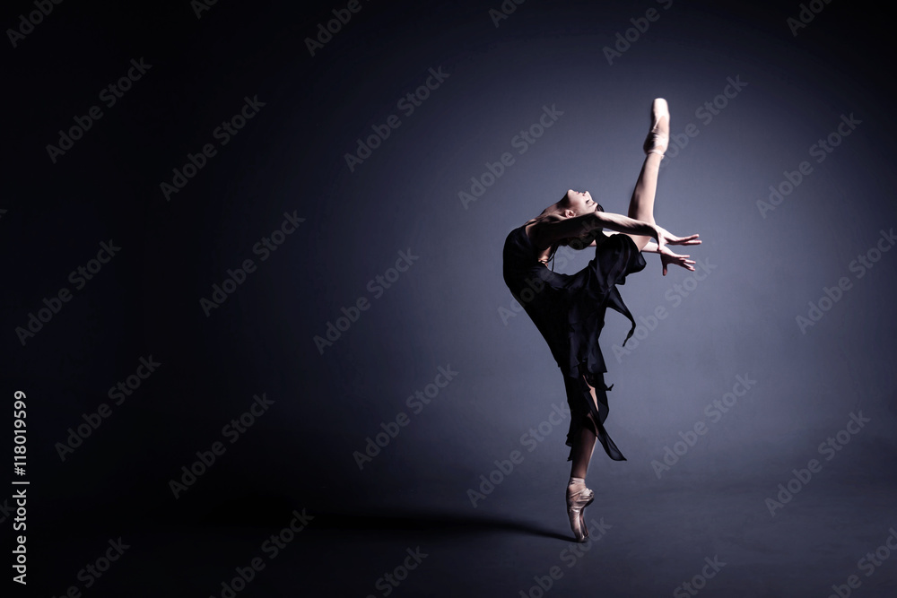 Young ballerina in a black suit is dancing in a dark studio - obrazy, fototapety, plakaty 