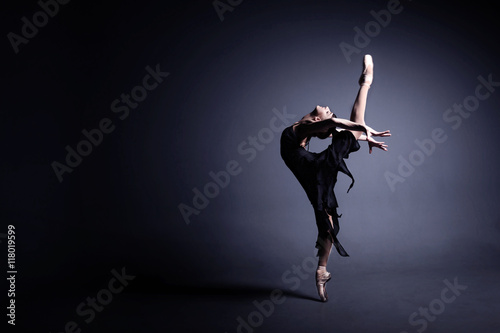 Fotótapéta Young ballerina in a black suit is dancing in a dark studio