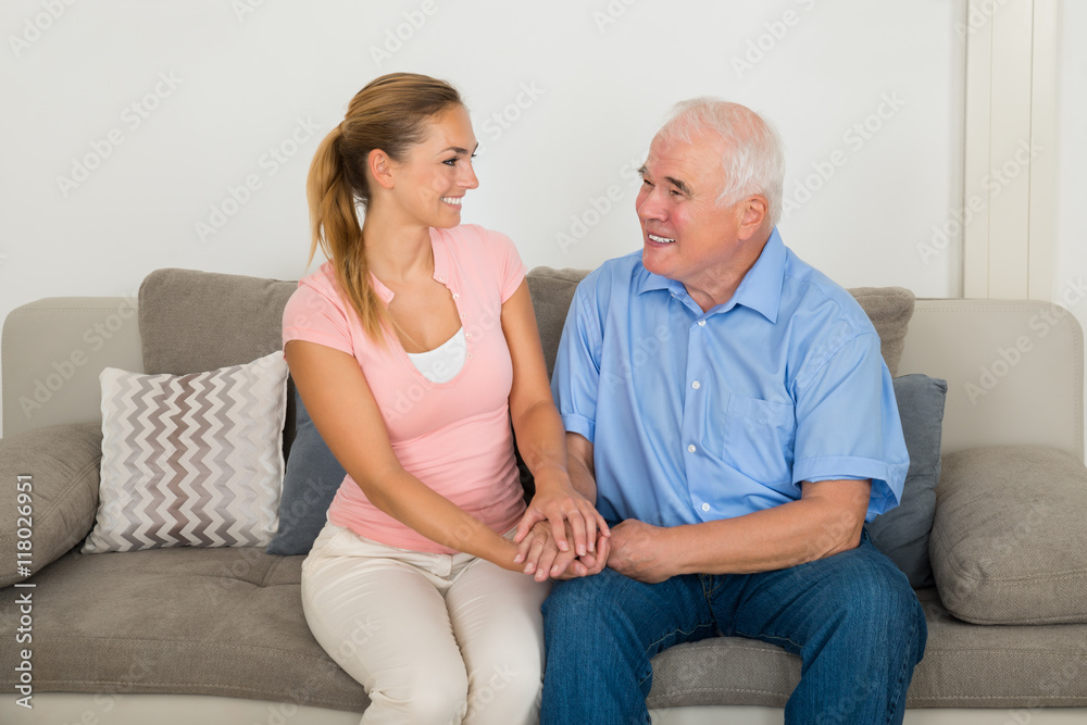 Woman Sitting On Sofa Holding Her Father's Hand